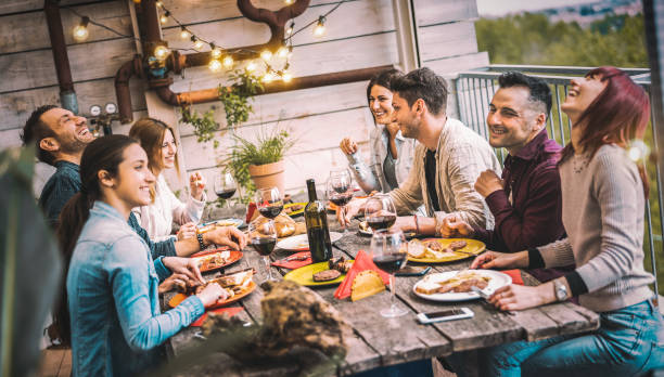 młodzi ludzie jedzący i bawiący się pijąc czerwone wino razem na balkonie na dachu kolacji - szczęśliwi przyjaciele jedzący dania z grilla na patio restauracji - koncepcja stylu życia millannial na ciepłym wieczornym filtrze - barbecue spotkanie towarzyskie zdjęcia i obrazy z banku zdjęć