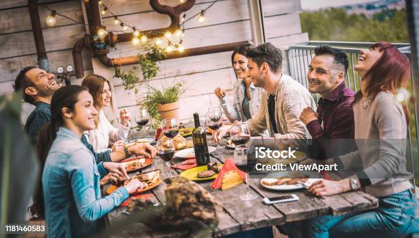 年輕人在陽臺屋頂晚宴上一起用餐和享受喝紅酒的樂趣 快樂的朋友在餐廳天井吃燒烤食品 在溫暖的晚間篩檢程式上享受 Millannial 生活方式概念 照片檔及更多 友誼 照片