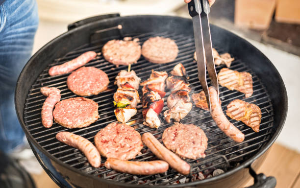 Close up of hand grilling meat at barbecue session - Skewers and burger sausages cooked on ember at bbq garden party - Pic nic concept with lunch outdoors on spring summer time - Warm vivid filter primer plano de la carne a la parrilla a mano en la sesión de barbacoa - pinchos y salchichas de hamburguesa cocinadas en ember en barbacoa jardín fiesta - pic nic concepto con almuerzo al aire libre en primavera verano - filtro cálido vívido