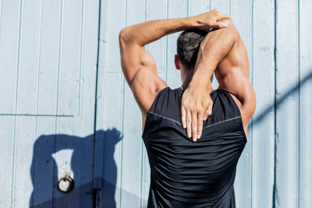 homem novo que estica de encontro a uma parede azul após um exercício - back rear view men muscular build - fotografias e filmes do acervo