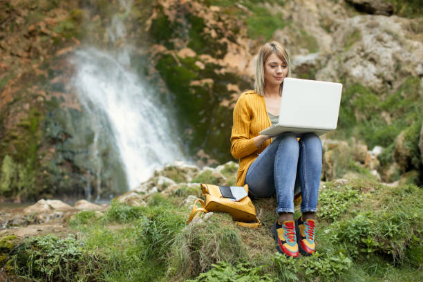 istock Young woman using laptop near waterfall 1181465780