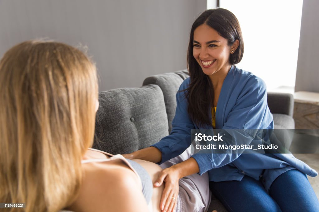 Midwife examining expectant mother Midwife examining expectant mother and satisfied with checkup. Young woman touching belly of pregnant patient lying on couch. Maternity and healthcare concept Midwife Stock Photo