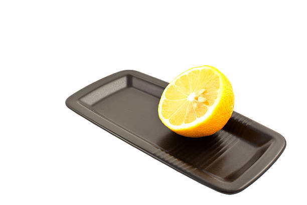 Yellow lemons with leaves on dark gray plate on wooden background