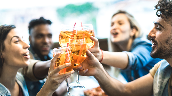 Amigos bebiendo spritz en el restaurante de la barra de cócteles de moda - Concepto de amistad con los jóvenes divirtiéndose juntos tostando bebidas en la hora feliz en el pub - Enfoque en el vidrio central - Filtro de naranja Teal photo