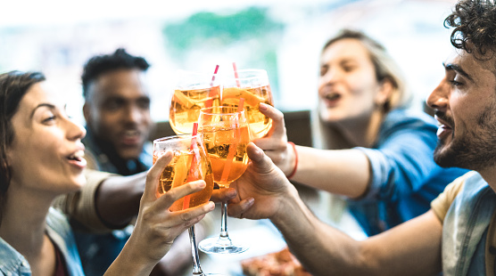 Friends drinking spritz at fashion cocktail bar restaurant - Friendship concept with young people having fun together toasting drinks on happy hour at pub - Focus on central glass - Teal orange filter