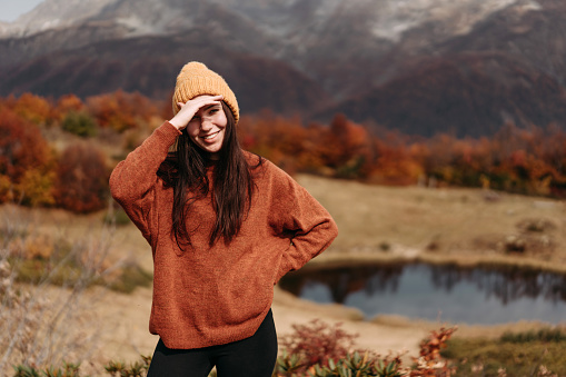 Cute young woman in a sweater and hat in the mountains by the lake in the autumn season.