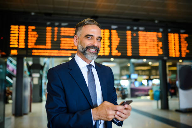 un hombre de negocios sonriente en el aeropuerto revisando el vuelo - airport business travel arrival departure board travel fotografías e imágenes de stock