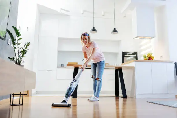 Photo of Full length of worthy caucasian blonde housewife using steamer to clean floor in living room.