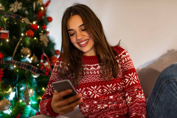 istock Woman texting on smartphone with christmas tree 1181498826