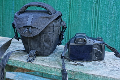 one black camera and bag stand on a gray table against a green wall