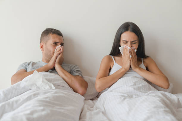 giovane coppia malata caucasica che si sente male insieme a causa del freddo sdraiato a letto a casa - cold and flu flu virus bed couple foto e immagini stock