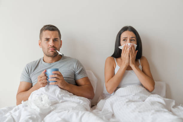 la coppia ha preso l'influenza e giaceva a letto a casa mentre prendeva temperatura e beveva tè di medicina dalla tazza - cold and flu flu virus bed couple foto e immagini stock