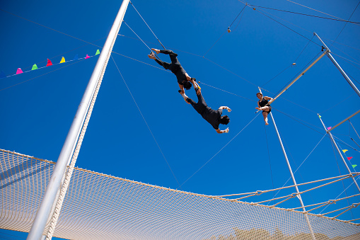 Three trapeze artists playing together in the blue sky