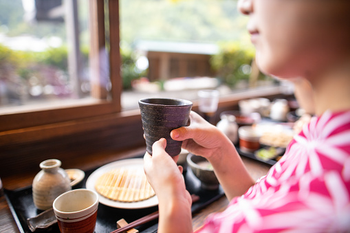 Young woman in yukata holding Japanese tea at Soba restaurant