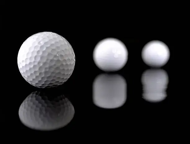 Three white golfballs on a black background. The ball in the front is very sharp, the other two not - strong depth of field