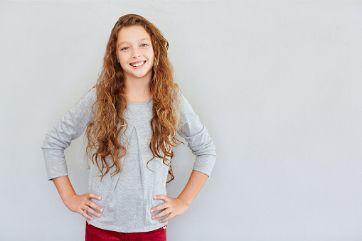 Portrait of a cute little girl with a big smile standing with her hands on her hips against a gray background