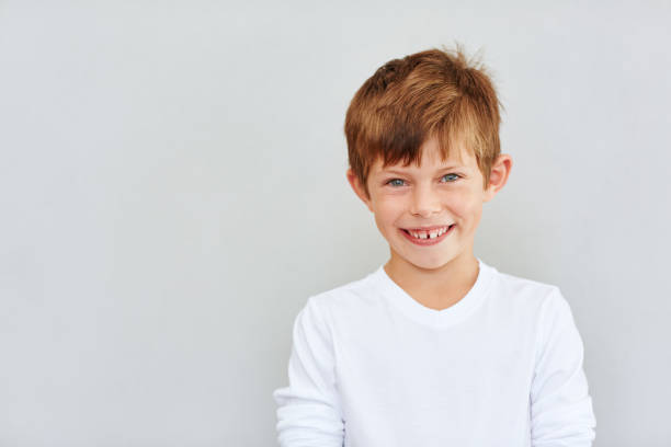 Portrait of a cute little boy with a big smile standing against a gray background