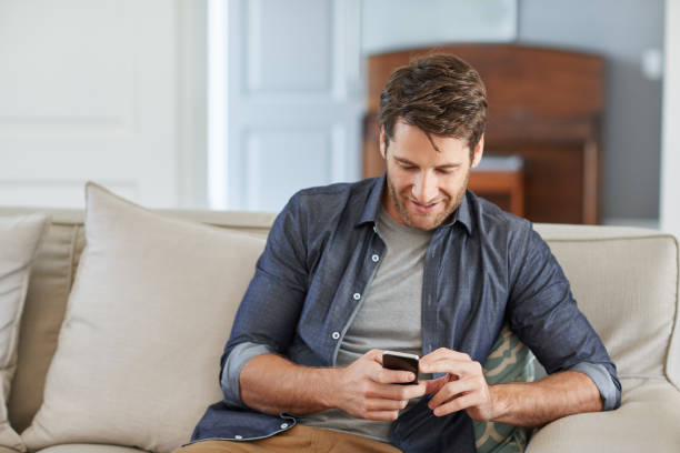 istock Smiling man reading a text on his sofa at home 1181530596