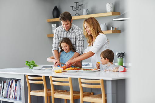 Smiling parents preparing lunch together with their two little children in their kitchen at home
