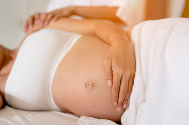 les femmes enceintes apprécient un massage relaxant dans le lit à la maison. traiter et soigner la santé mentale du fœtus concept de soins prénatals et de grossesse des femmes - abdomen women massaging human hand photos et images de collection