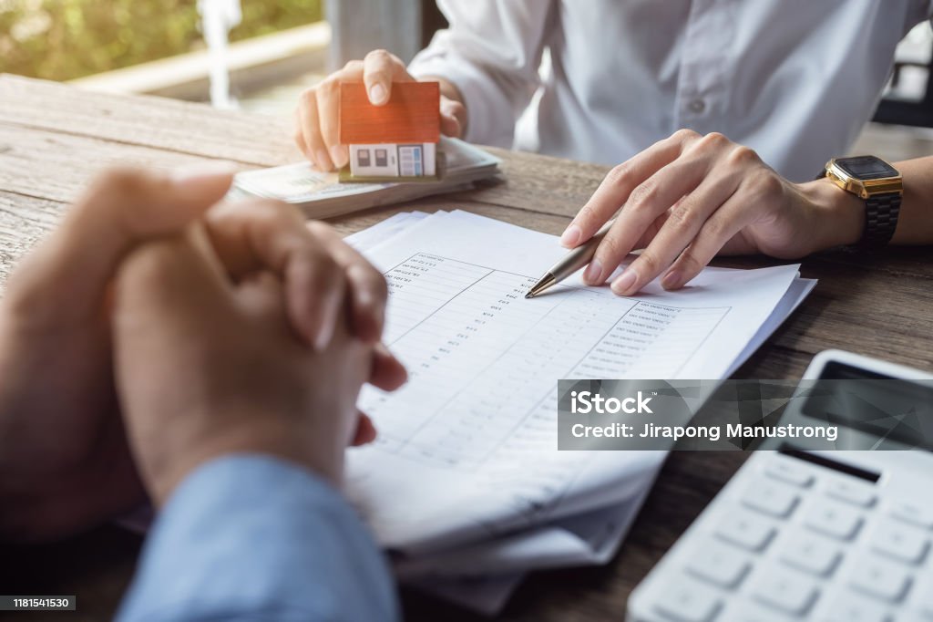 Loan agreement, real estate agent or bank officer describes the loan interest to the customer, along with loan documents with a home-style pen and a replica money on a wooden table. Fee Stock Photo