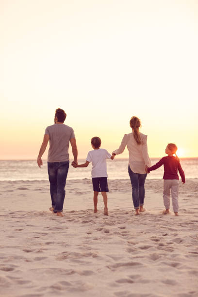 istock Family holding hands while walking along a beach at sunset 1181542271