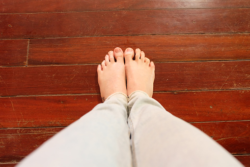 Selfie of feet in fashion bare feet on wooden background from above. Top view. Beauty and fashion concept. Beautiful woman wearing blue jeans standing on wood floor. Foot and legs.