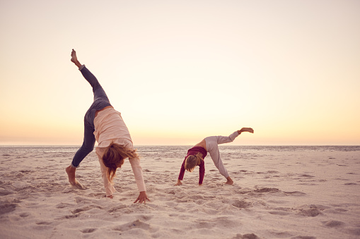 Mother and her little daughter doing cartwheels together while having fun on a sandy beach at sunset