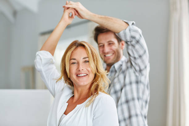 pareja sonriente cogidos de la mano y bailando juntos en casa - pareja de mediana edad fotografías e imágenes de stock