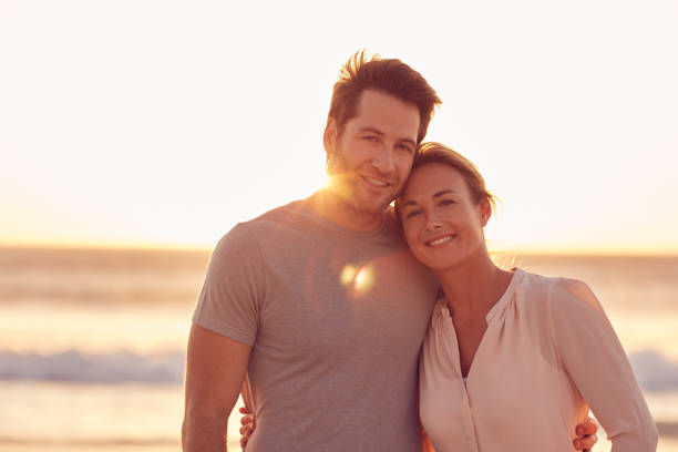 istock Smiling couple standing together on a beach at sunset 1181544448