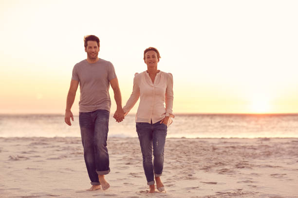 istock Smiling couple holding hands together on a beach at sunset 1181545352