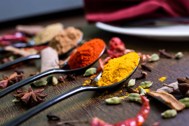 ensemble de diverses épices décorées sur la cuillère et l'assiette de dîner placées sur une table en bois foncé. poivre froid, romarin, basilic, curcuma, paprika, ail, anis, cannelle et autres. - spice ayurveda herb curry powder photos et images de collection