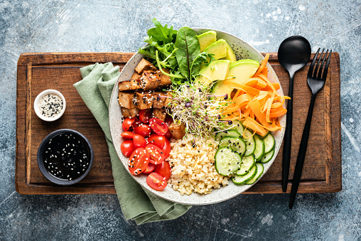 Buddha bowl with tofu, avocado, bulgur grains, cucumber, carrot and tomato garnished with seeds and micro greens. Healthy vegan and vegetarian food, tasty lunch or meal. Top view salad bowl