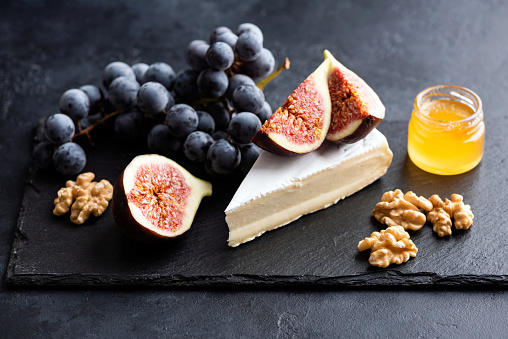 Brie or camembert cheese board with walnuts, grapes, figs and honey served on black slate plate. Gourmet appetizer