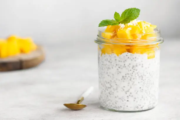 Chia pudding with mango in jar on grey concrete background. Clean eating concept, healthy vegetarian food