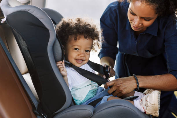 一個快樂的小男孩看著相機的側面視圖，而他的母親在汽車座椅上屈曲他 - 嬰兒安全座椅 圖片 個照片及圖片檔