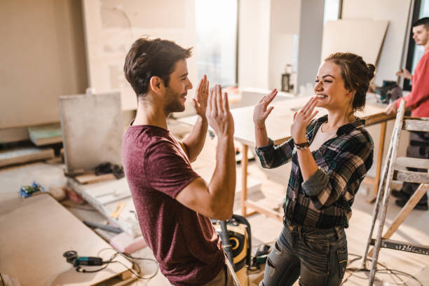 Happy couple giving each other high-five at their renovating apartment. Young happy couple standing at construction site inside of their apartment and giving each other high-five. diy stock pictures, royalty-free photos & images
