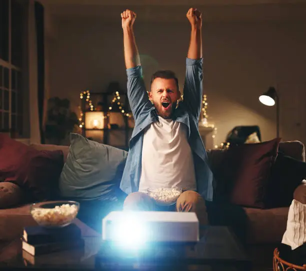 Photo of young male cheerleader watching football on tv projector at home in evening