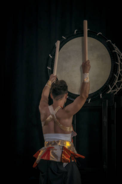 el baterista de taiko golpea el tambor grande en el escenario en un fondo negro, vista posterior. - taiko drum fotografías e imágenes de stock