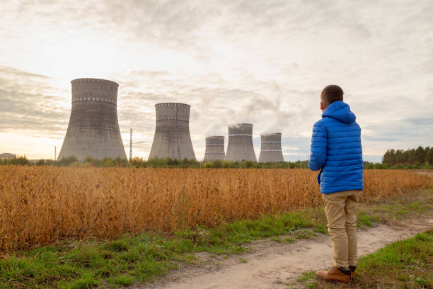 o menino olha a cena com chaminés da central energética nuclear. conceito de perspectivas de energia nuclear. - nuclear power station nuclear energy child nuclear reactor - fotografias e filmes do acervo