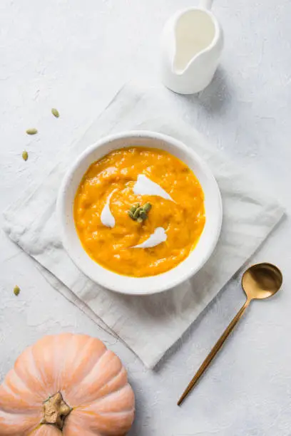 Photo of Pumpkin soup with cream on grey stone background. Top view.