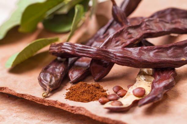 johannisbrot. bio-karob hülsen mit samen und blättern auf baumrindentisch. gesunde ernährung, essen hintergrund. - carob bean stock-fotos und bilder