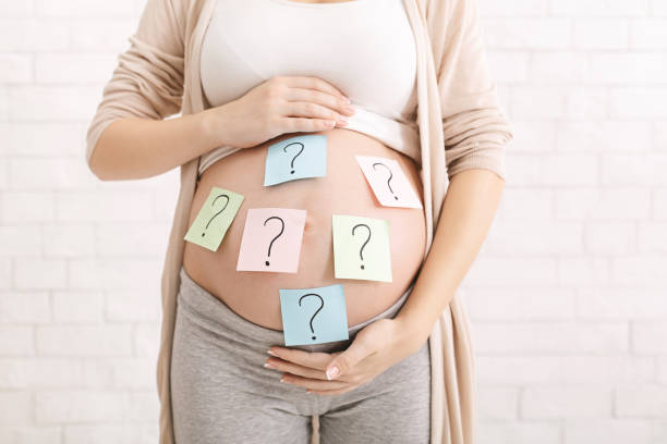 Confused pregnant woman with question marks on paper stickers on tummy Choosing baby name. Confused pregnant woman with question marks on paper stickers on tummy pregnancy and childbirth stock pictures, royalty-free photos & images