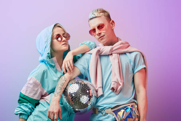 joven pareja de bailarines de moda posando con bola de discoteca sobre fondo violeta - women sunglasses little girls glamour fotografías e imágenes de stock