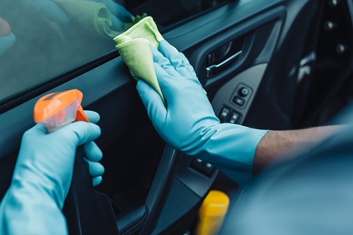vista recortada del limpiador de automóviles sosteniendo el trapo y la botella de spray mientras limpia la puerta del coche photo