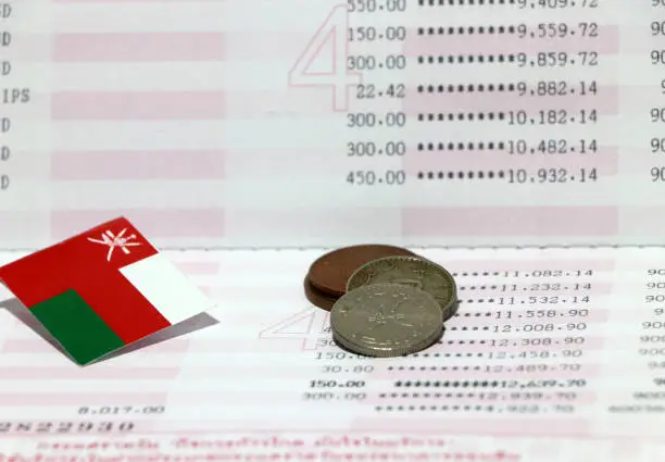 Four coins of Rial Omani money with mini Oman flag on the book bank. Concept of Saving money or finance.