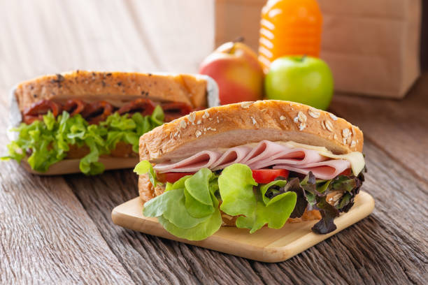 サンドイッチハムとチーズ、トマト、レタス、全粒パンとサラミサンドイッチ。オレンジジュースとリンゴの茶色の紙のランチ。 - club sandwich sandwich salad bread ストックフォトと画像