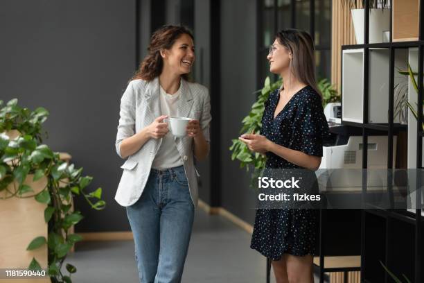 Asian And Caucasian Ethnicity Women Colleagues Chatting In Office Hallway - Fotografias de stock e mais imagens de Discussão