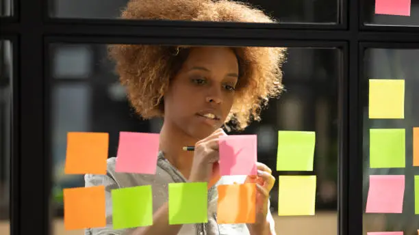 Photo of African woman writing down on sticky notes view through glass