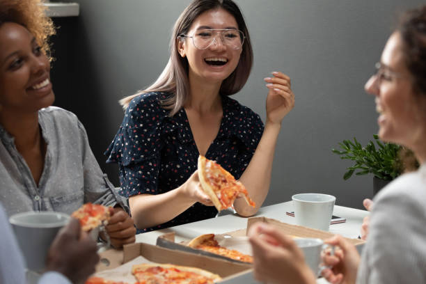 Asian employee eat pizza seated with mates at lunch break Asian office worker eat pizza seated with mates at lunch break, multiethnic people having warm relationships friendly good relations, team building multi-racial friendship, enjoy meal together concept office buddies stock pictures, royalty-free photos & images